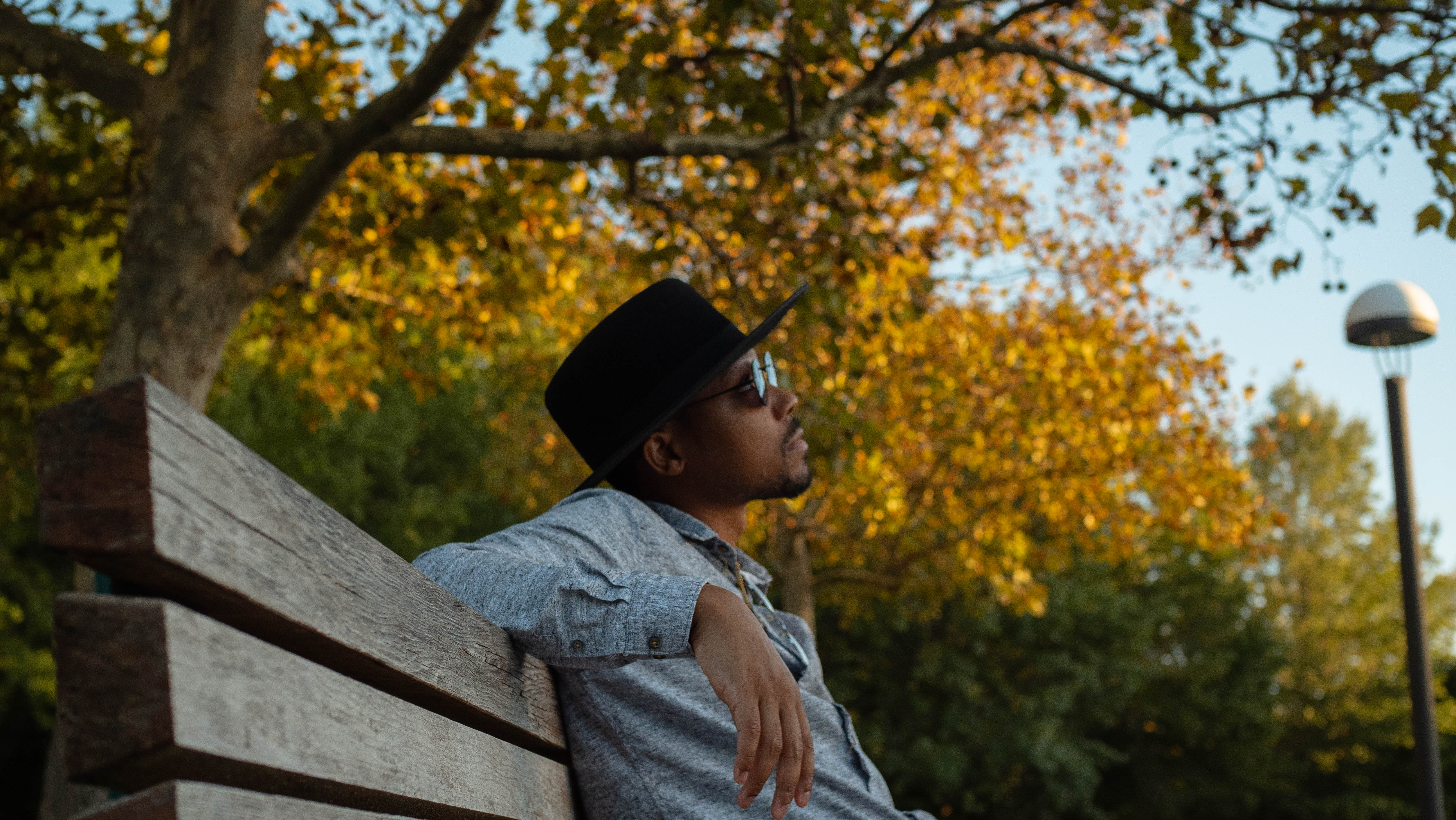 Kasper Brightside, in a black hat and sunglasses, seated outdoors against autumn foliage